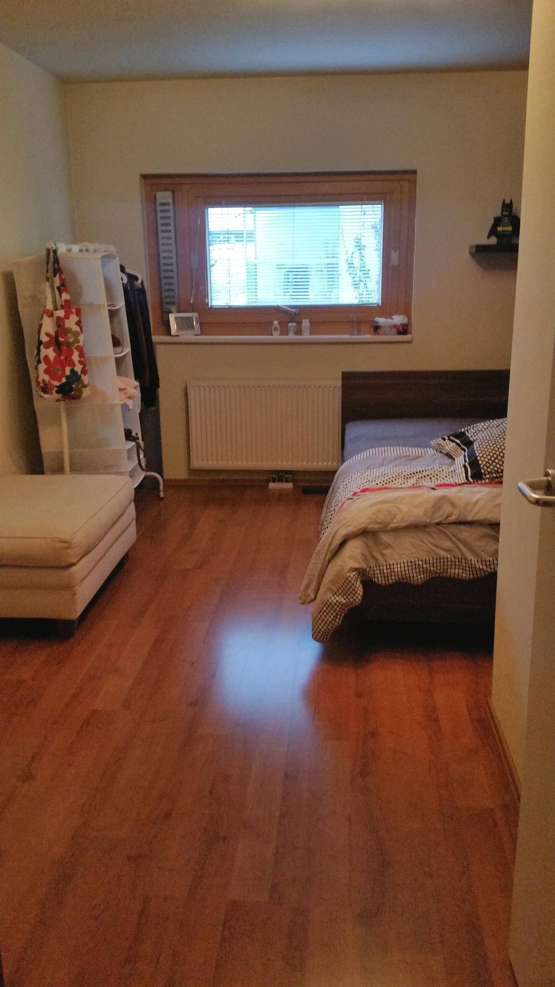 Schlafzimmer mit Holzboden, Bett und einem Fenster, das viel Tageslicht hereinlässt.