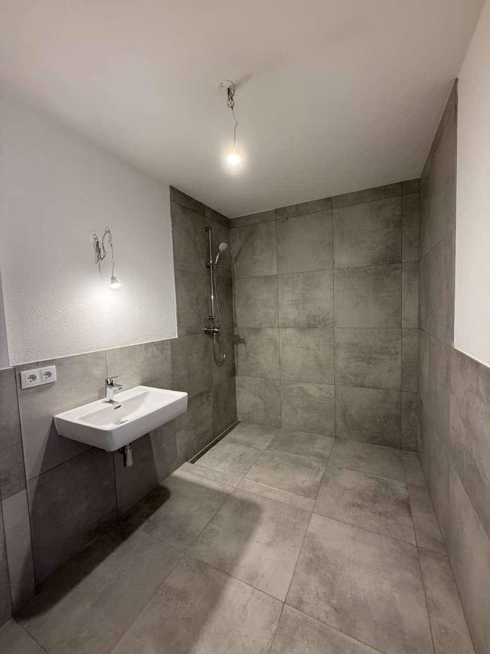 Zeitgemäßes Badezimmer mit großformatigen grauen Fliesen, modernem Waschbecken und Dusche.