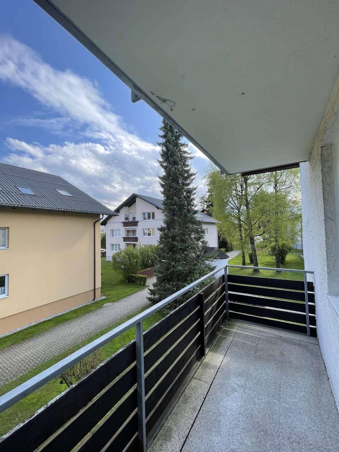 Balkon mit Blick auf die grüne Umgebung und benachbarte Gebäude unter blauem Himmel.