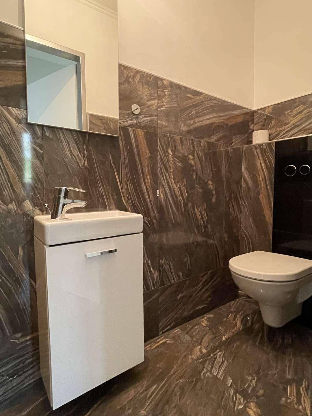 Modernes Gäste-WC mit dunklen Marmorfliesen, wandhängendem WC und kleinem Waschbecken.