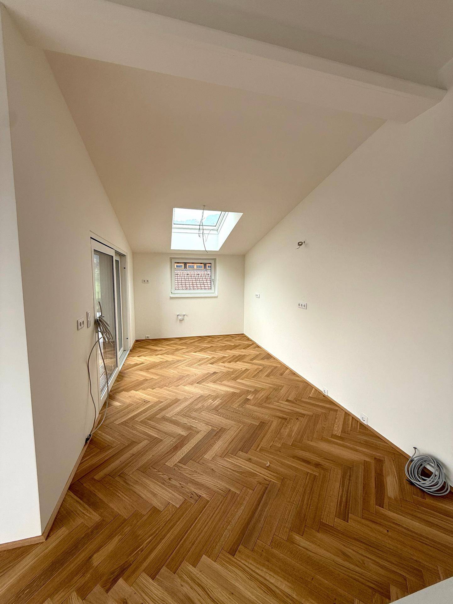 Helles Schlafzimmer mit Fischgrätparkett, Dachschräge und einem praktischen Dachfenster.