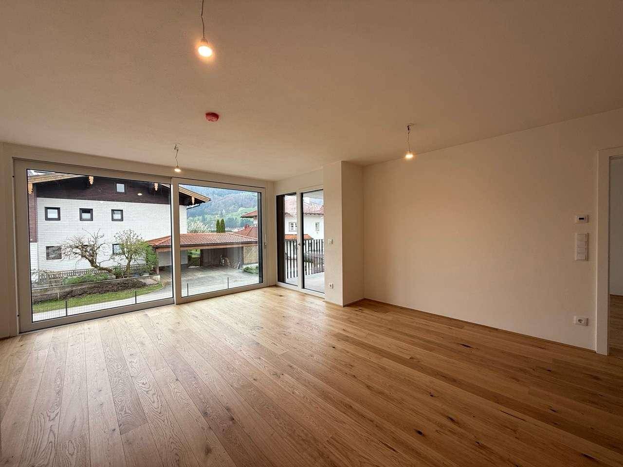 Lichtdurchfluteter Wohnraum mit Parkettboden und Zugang zu einem Balkon mit Bergsicht.
