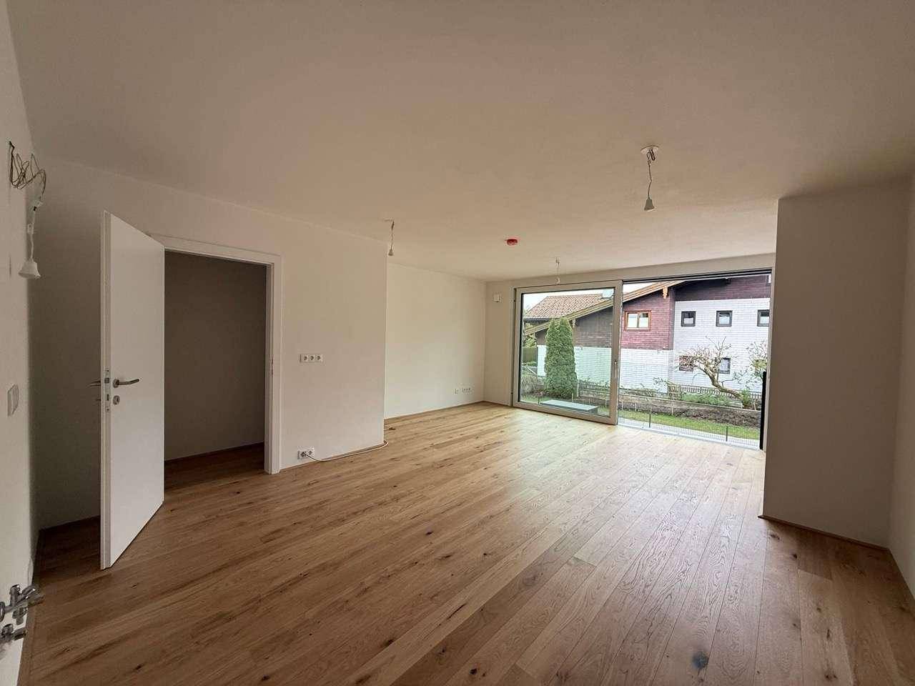 Heller Wohnbereich mit Holzboden und großen Fenstern, die einen Blick auf den Garten ermöglichen.