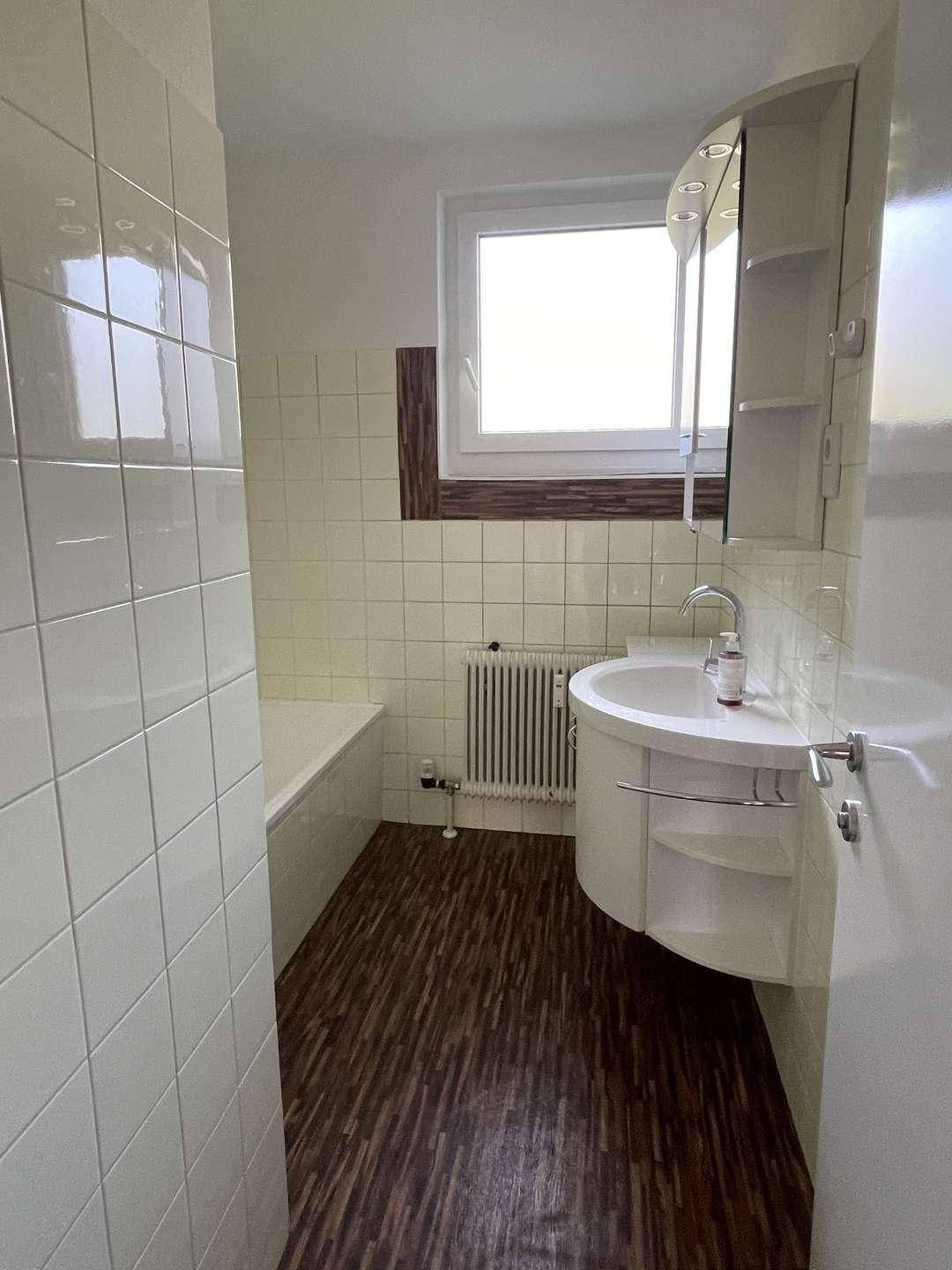 Badezimmer mit Badewanne, Waschbecken und Spiegelschrank, ausgestattet mit hellen Fliesen und Fenster.