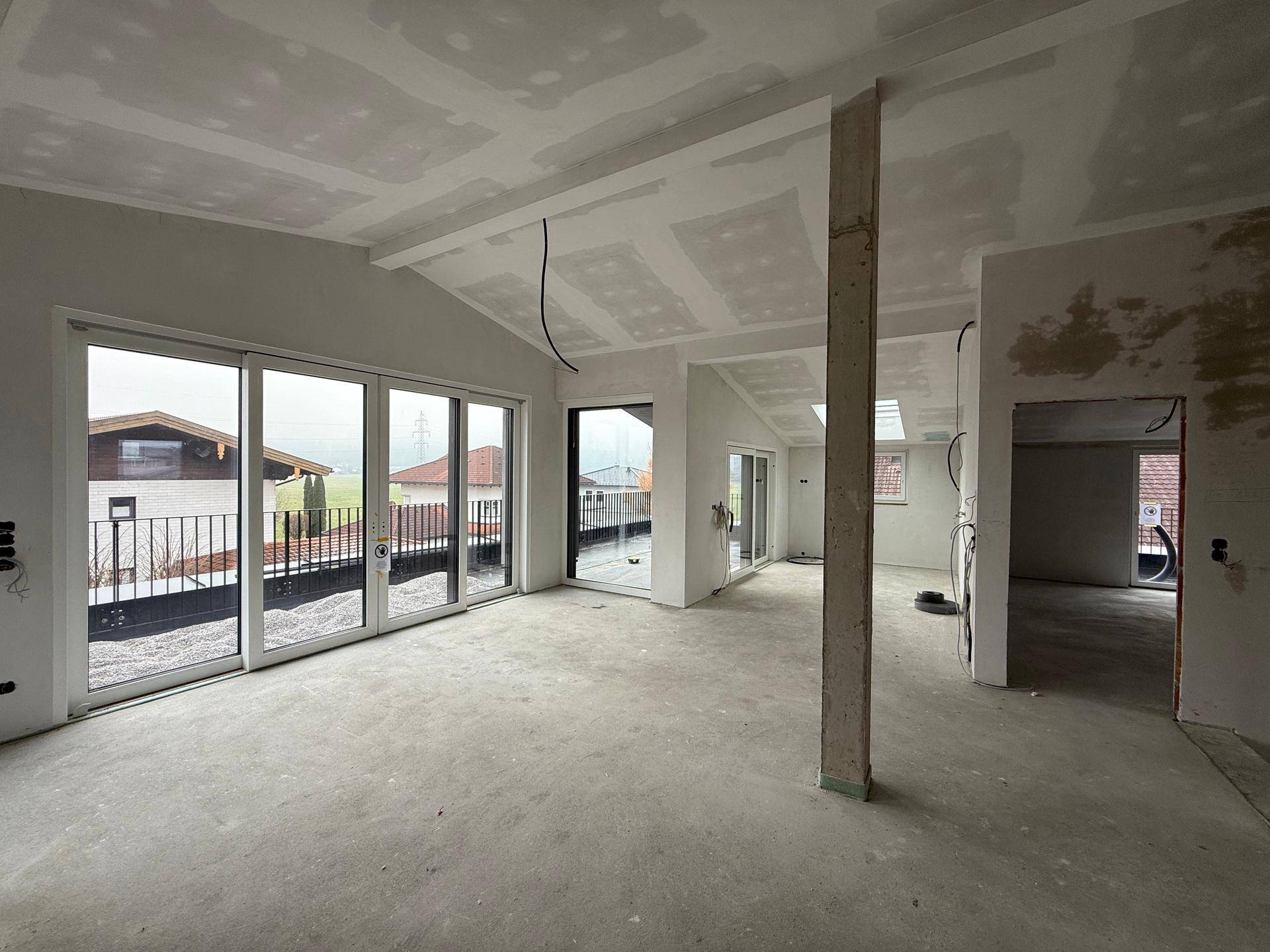 Heller, unfertiger Raum mit großen Fenstern, die Zugang zu einer Außenterrasse bieten.