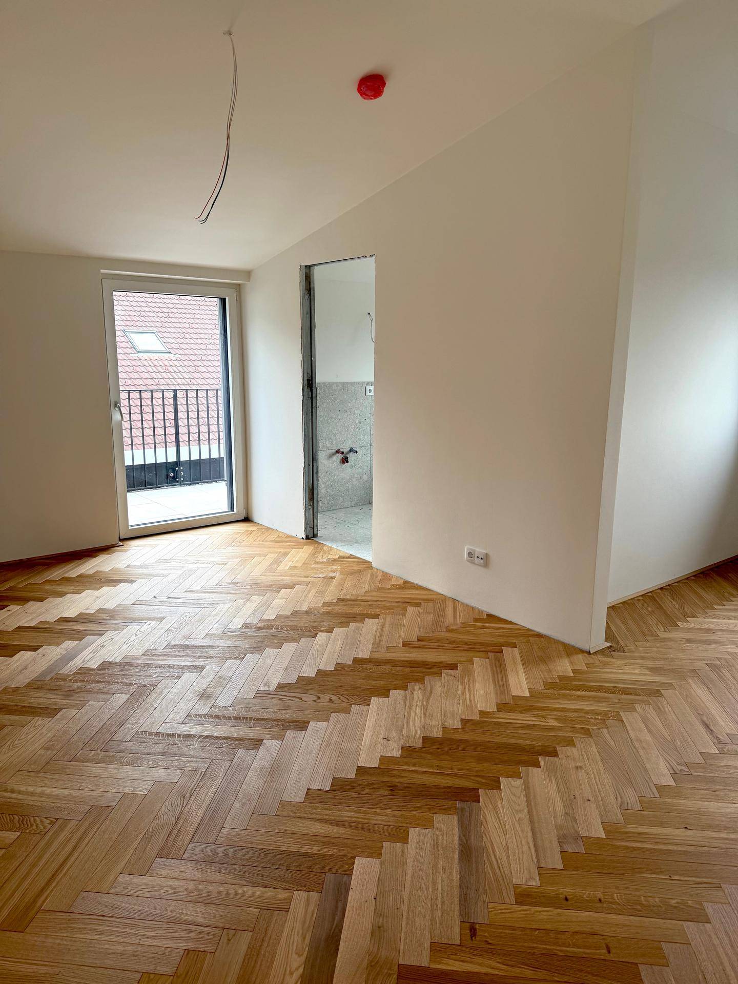 Schlafzimmer mit Fischgrätparkett, Zugang zum Badezimmer und einem kleinen Balkon.