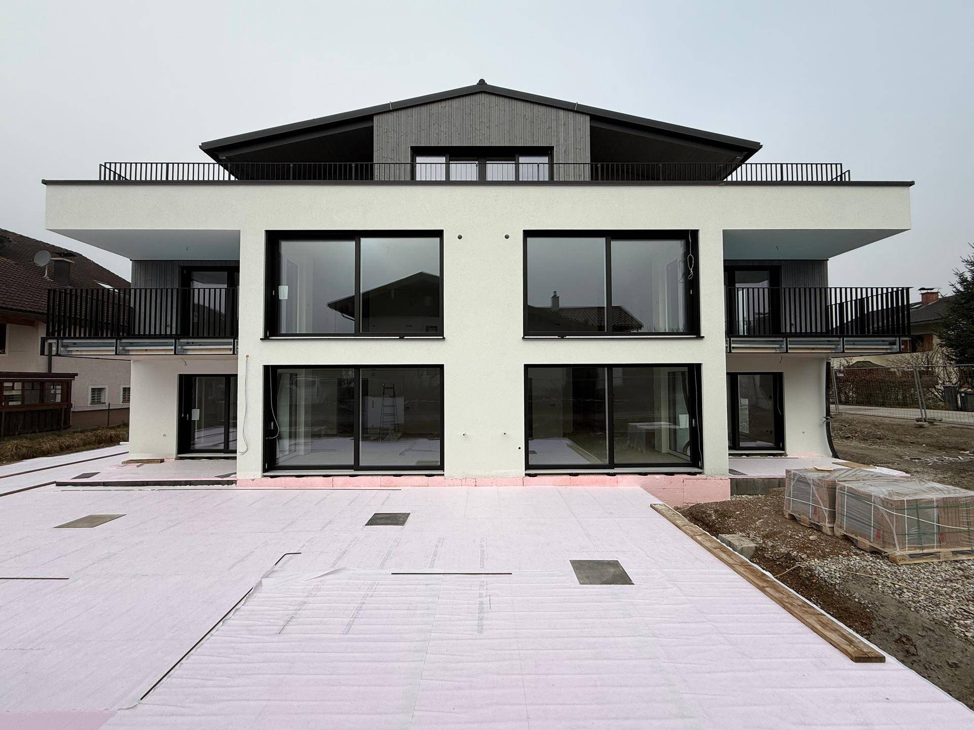 Moderne Fassade eines Neubaus mit großen Fenstern und Balkonen, umgeben von Baustellenmaterial.