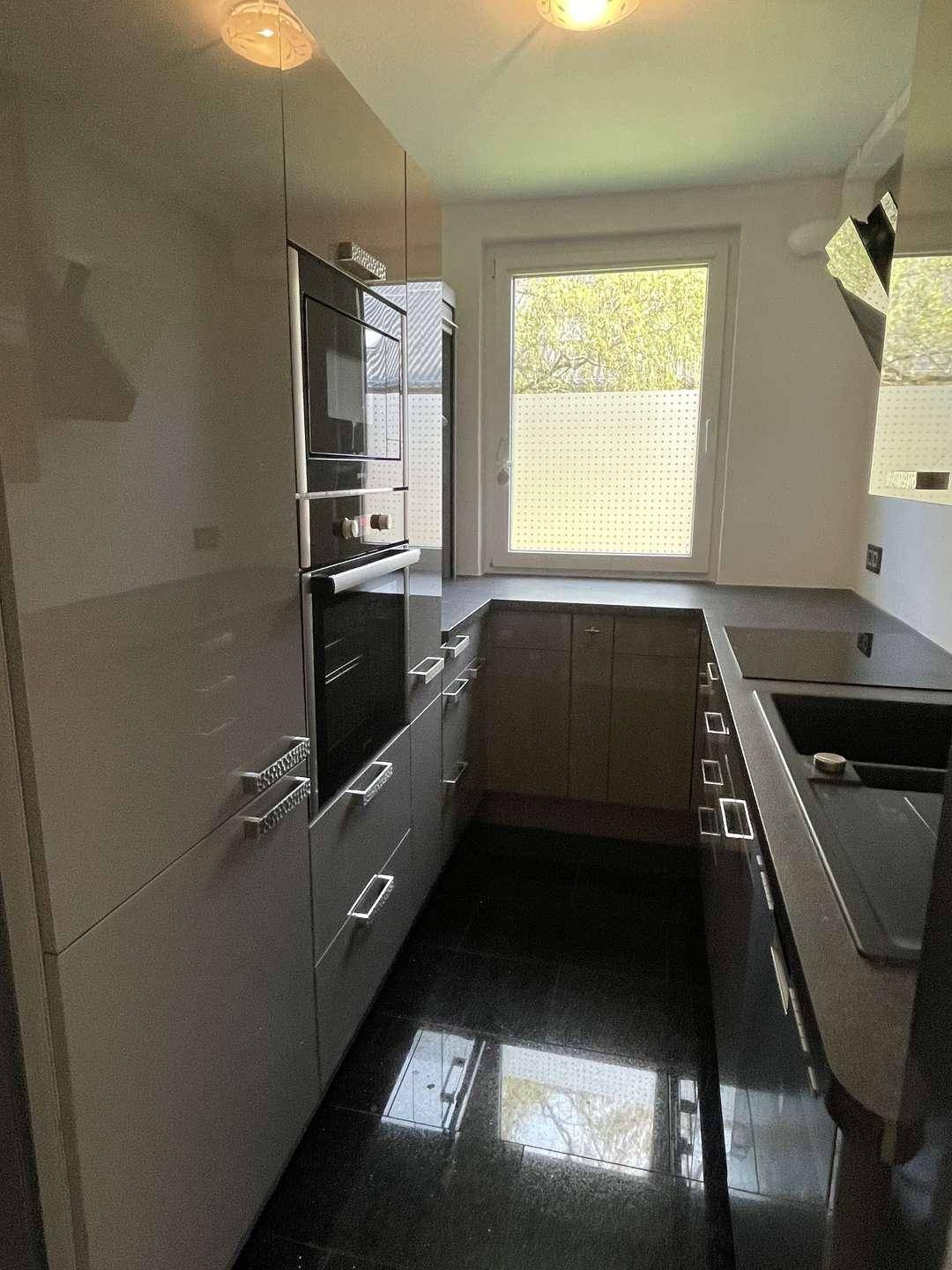 Moderne Küche mit glänzenden grauen Fronten, integrierten Geräten und dunklem Fliesenboden.