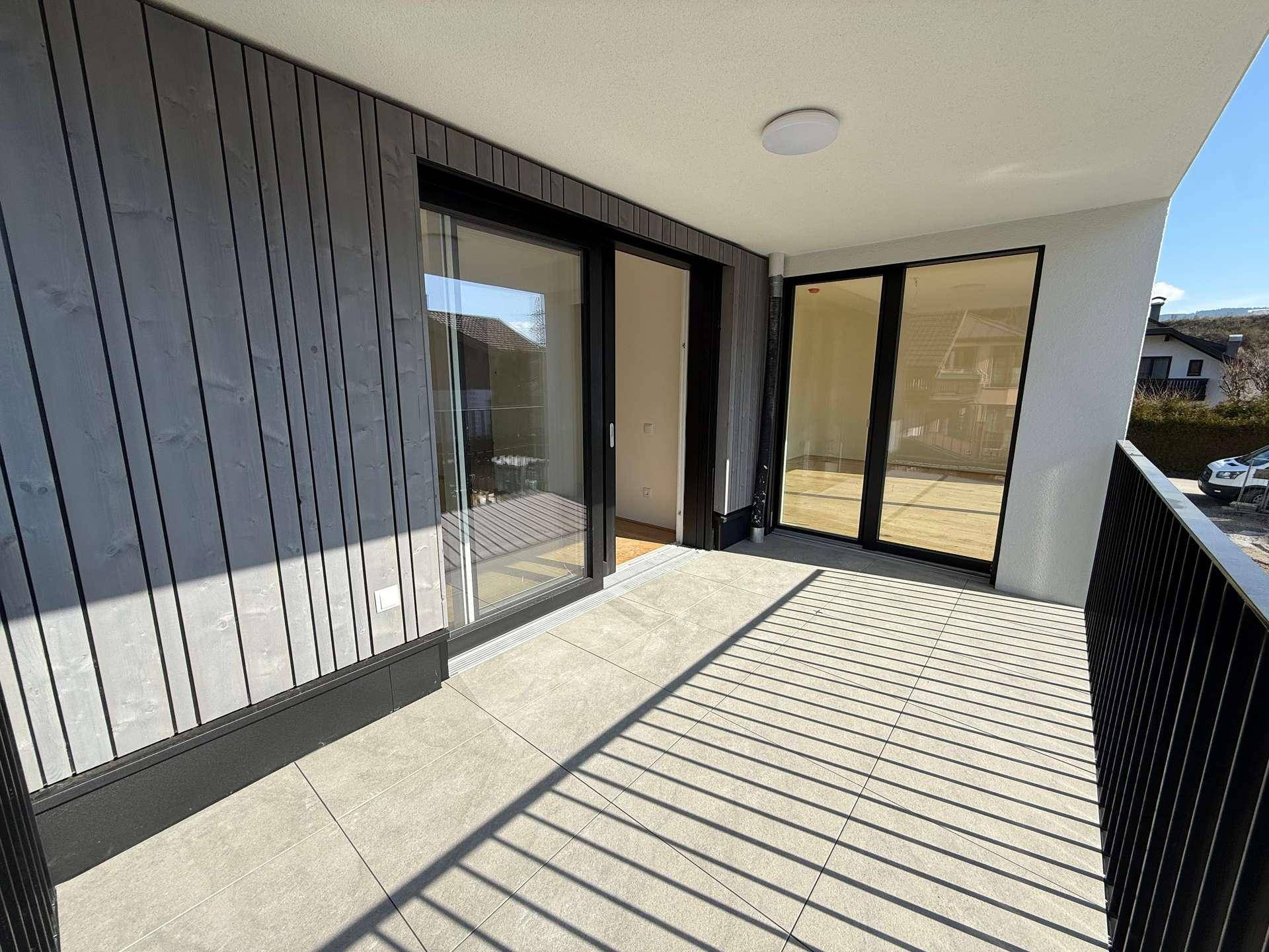 Sonniger Balkon mit Fliesenboden und Holzverkleidung, bietet Zugang zu den Innenräumen.