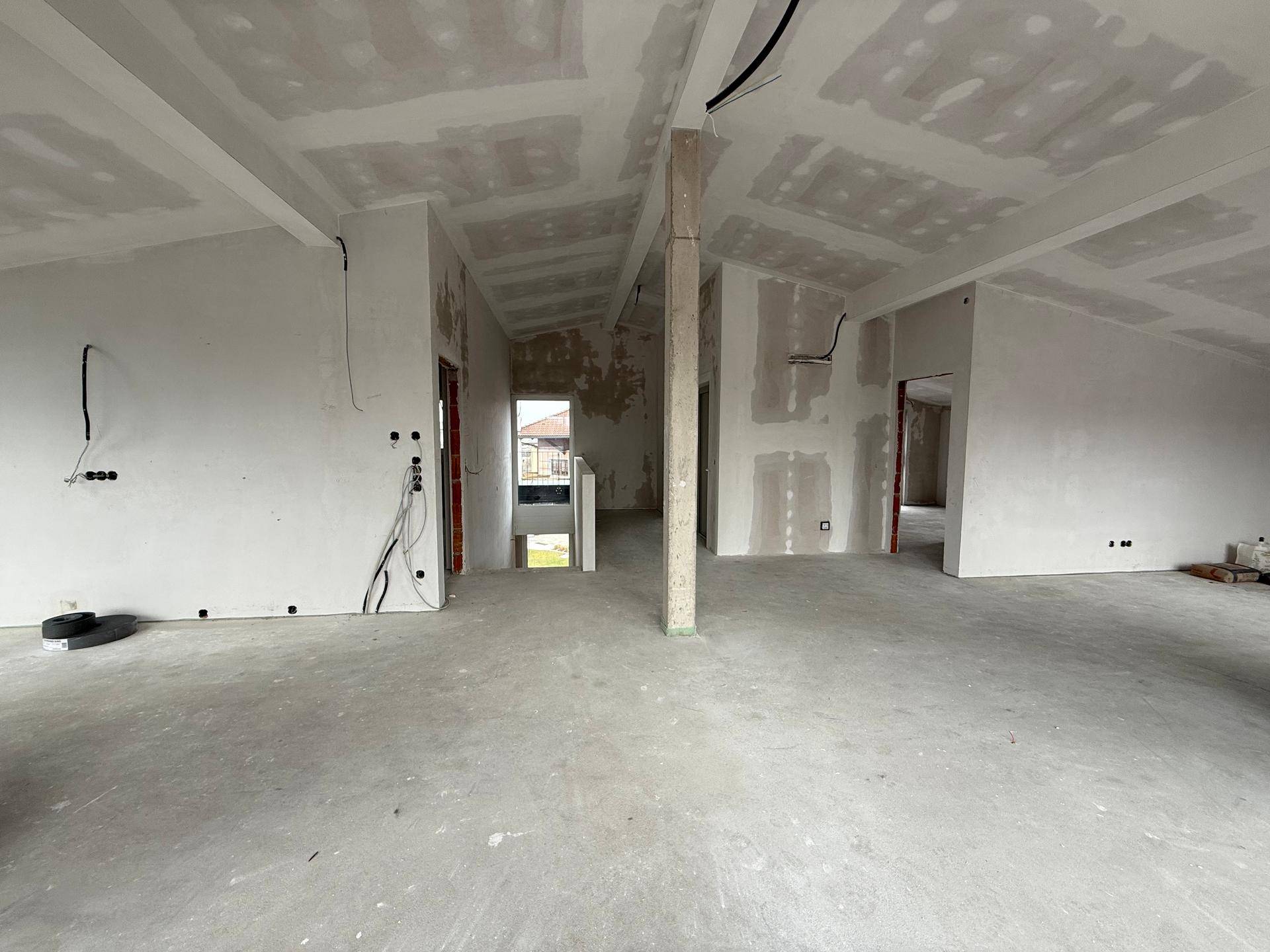 Unfertiger Innenraum mit Betonboden, schrägen Decken und sichtbaren Installationsvorbereitungen.