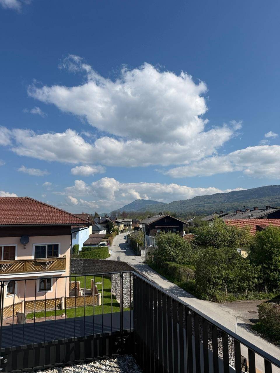 Blick von einem Balkon auf eine ruhige Wohnstraße und die entfernten Berge.