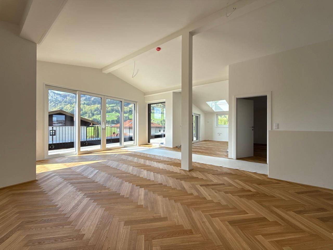 Geräumiges Wohnzimmer mit Fischgrätparkett, hohen Decken und Zugang zu einem Balkon.