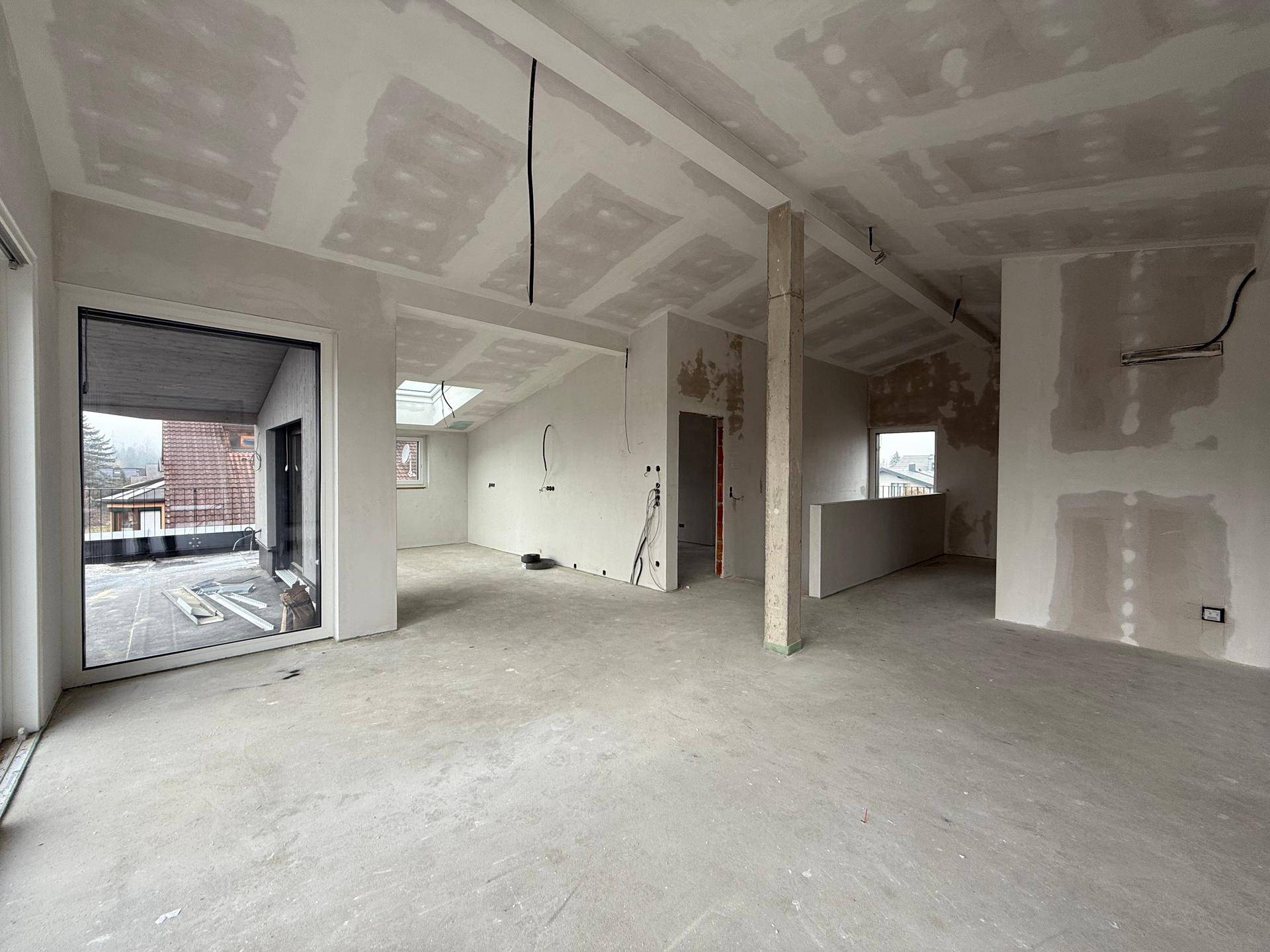 Großer, unfertiger Raum mit schrägen Decken, Betonboden und Zugang zu einer Terrasse.