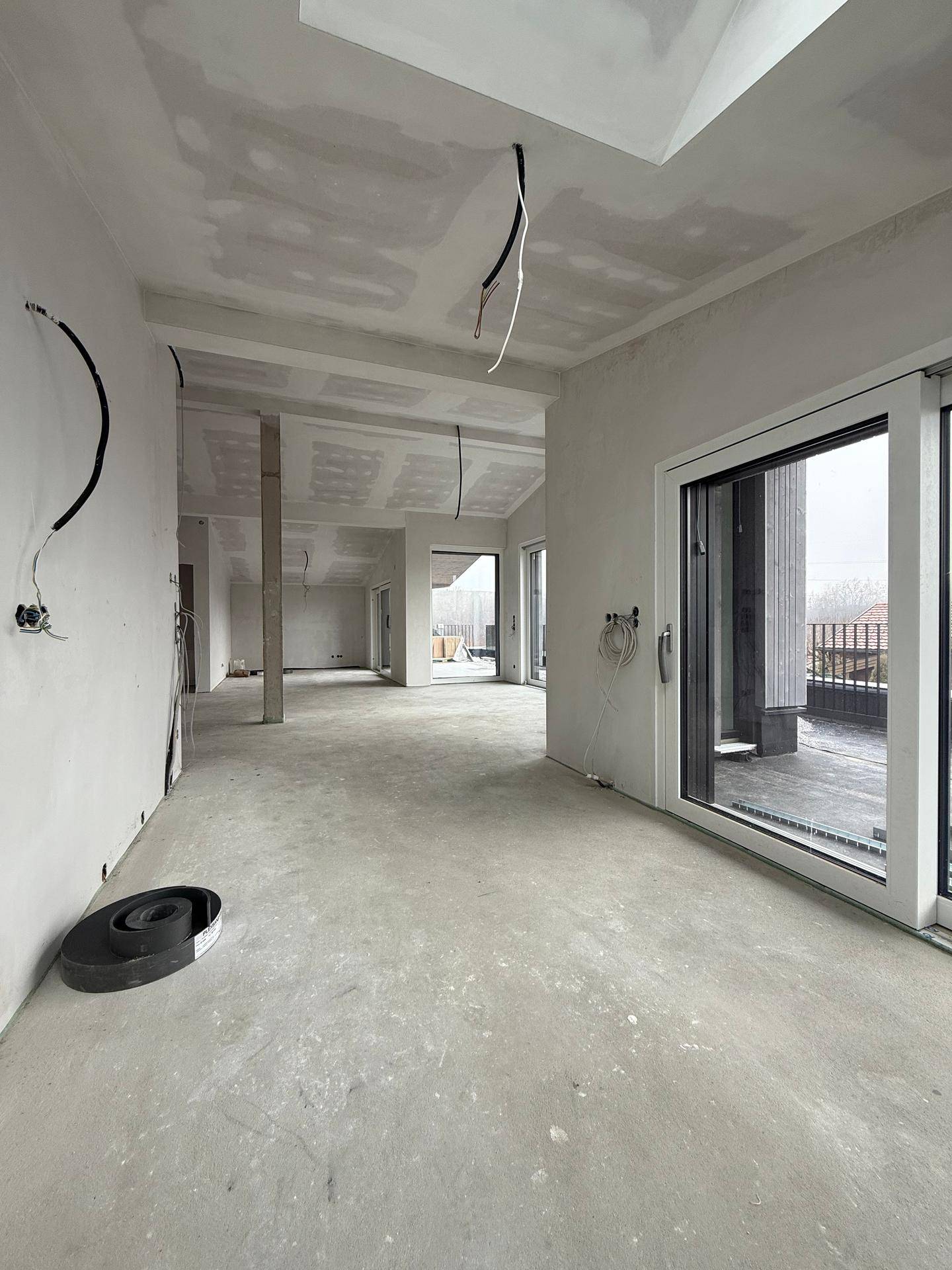 Geräumiger, unfertiger Innenraum mit Betonboden, schrägen Decken und großen Schiebetüren zur Terrasse.