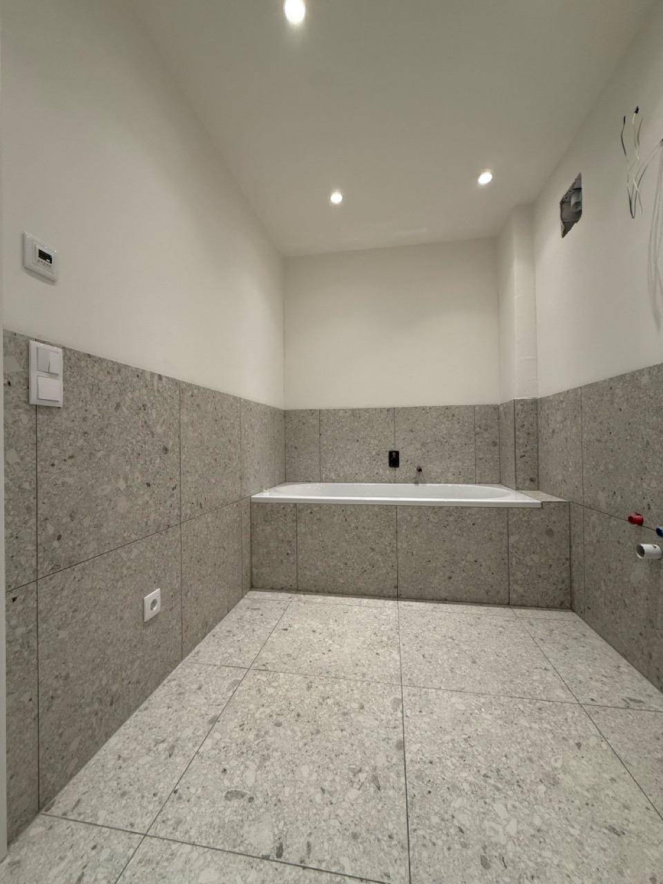 Badezimmer im Bau mit grauen Fliesen und einer bereits installierten Badewanne.