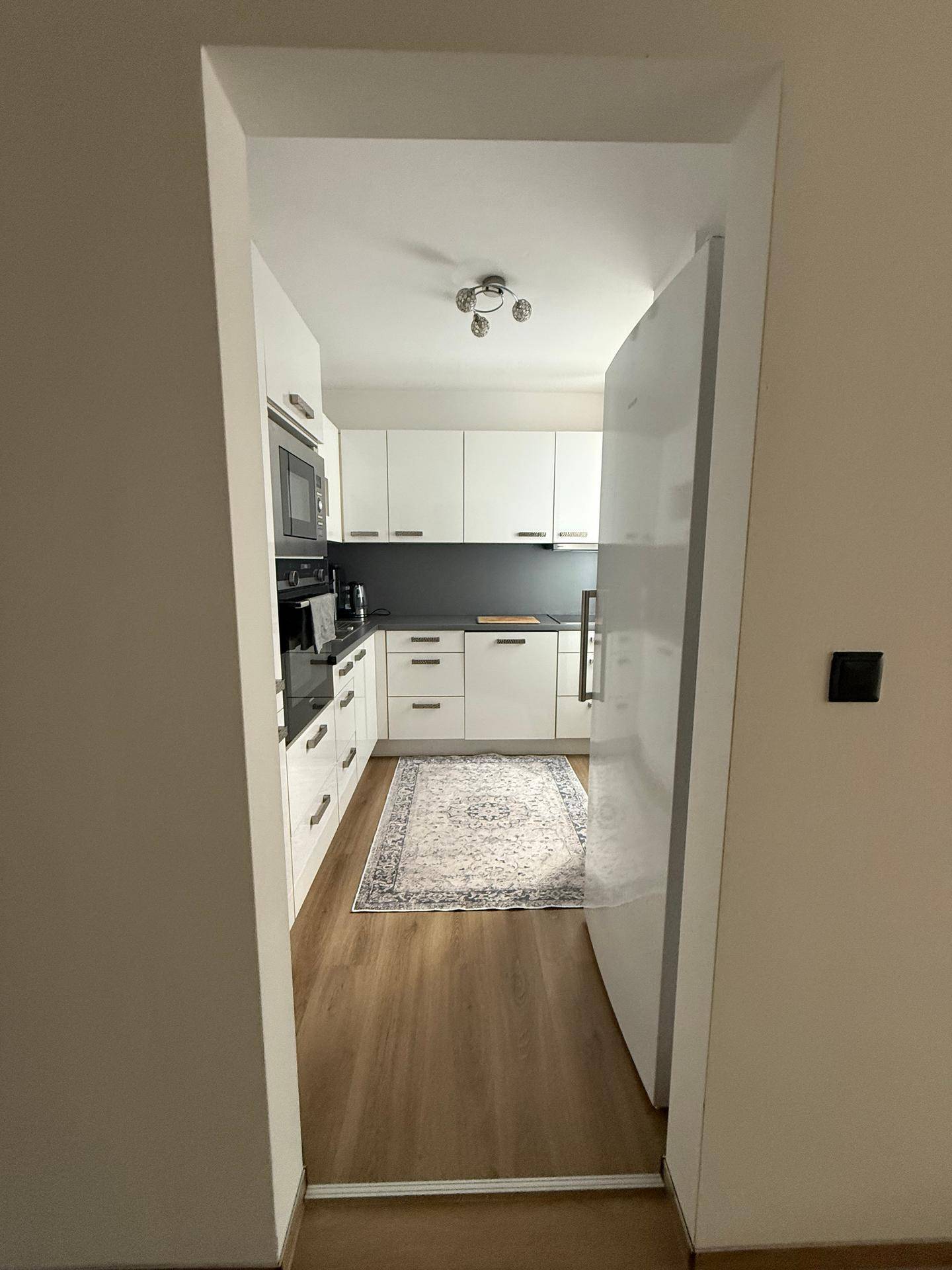 Moderne Küche mit weißen Schränken, dunkler Arbeitsplatte und Holzboden.