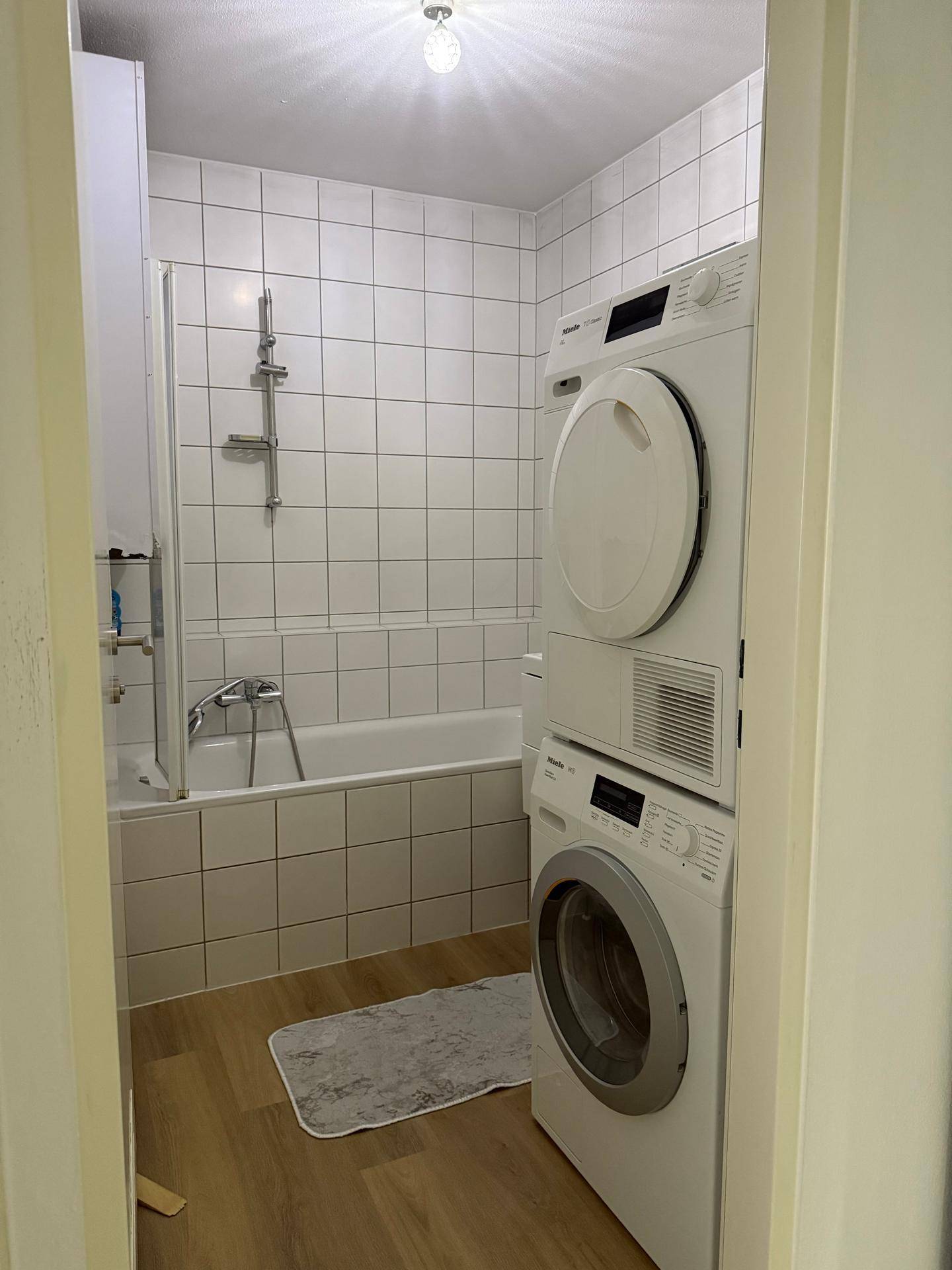Badezimmer mit Badewanne, Waschmaschine und Trockner sowie weißen Fliesen.