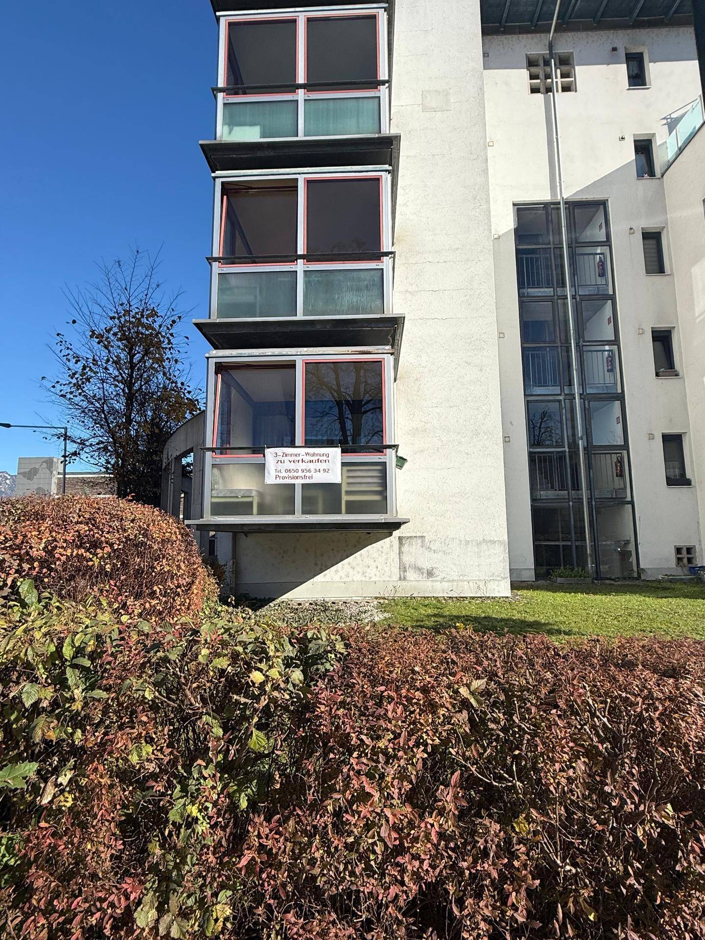 Mehrfamilienhaus mit mehreren verglasten Balkonen und gepflegter Außenanlage.