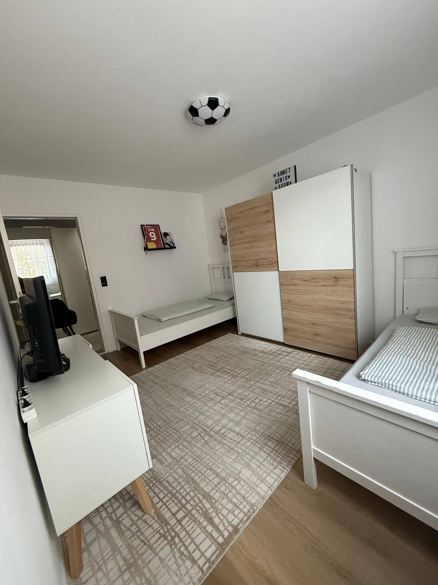 Helles Kinderzimmer mit zwei Betten, Schrank und Blick nach draußen.