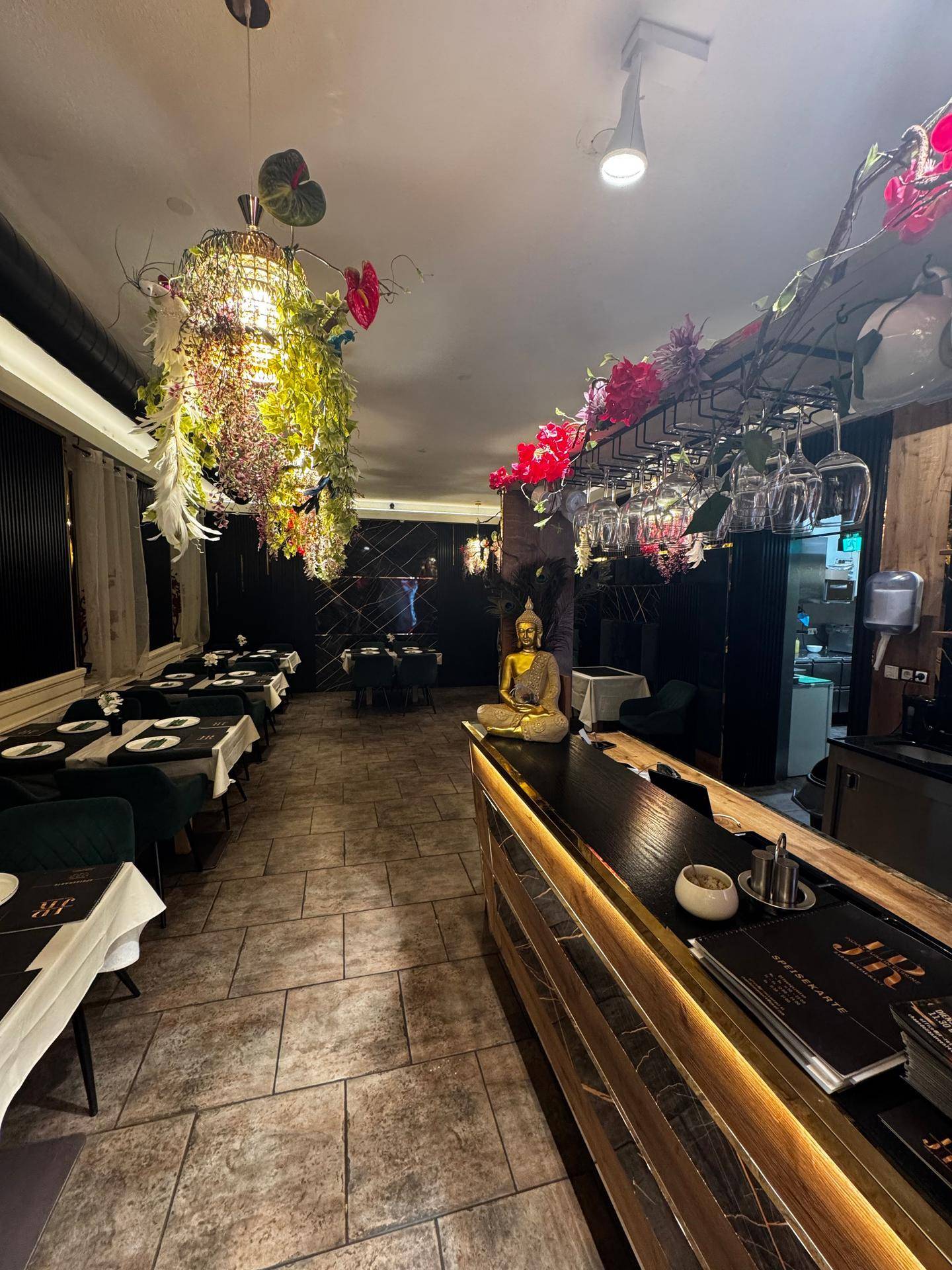 Blick auf die Bar und den Essbereich mit einer Buddha-Statue und floralen Hängelampen als Dekoration.