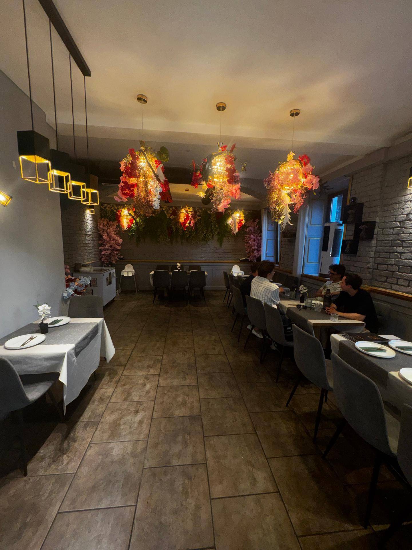 Restaurantraum mit gedeckten Tischen, floralen Hängelampen und einer einladenden Atmosphäre für Gäste.