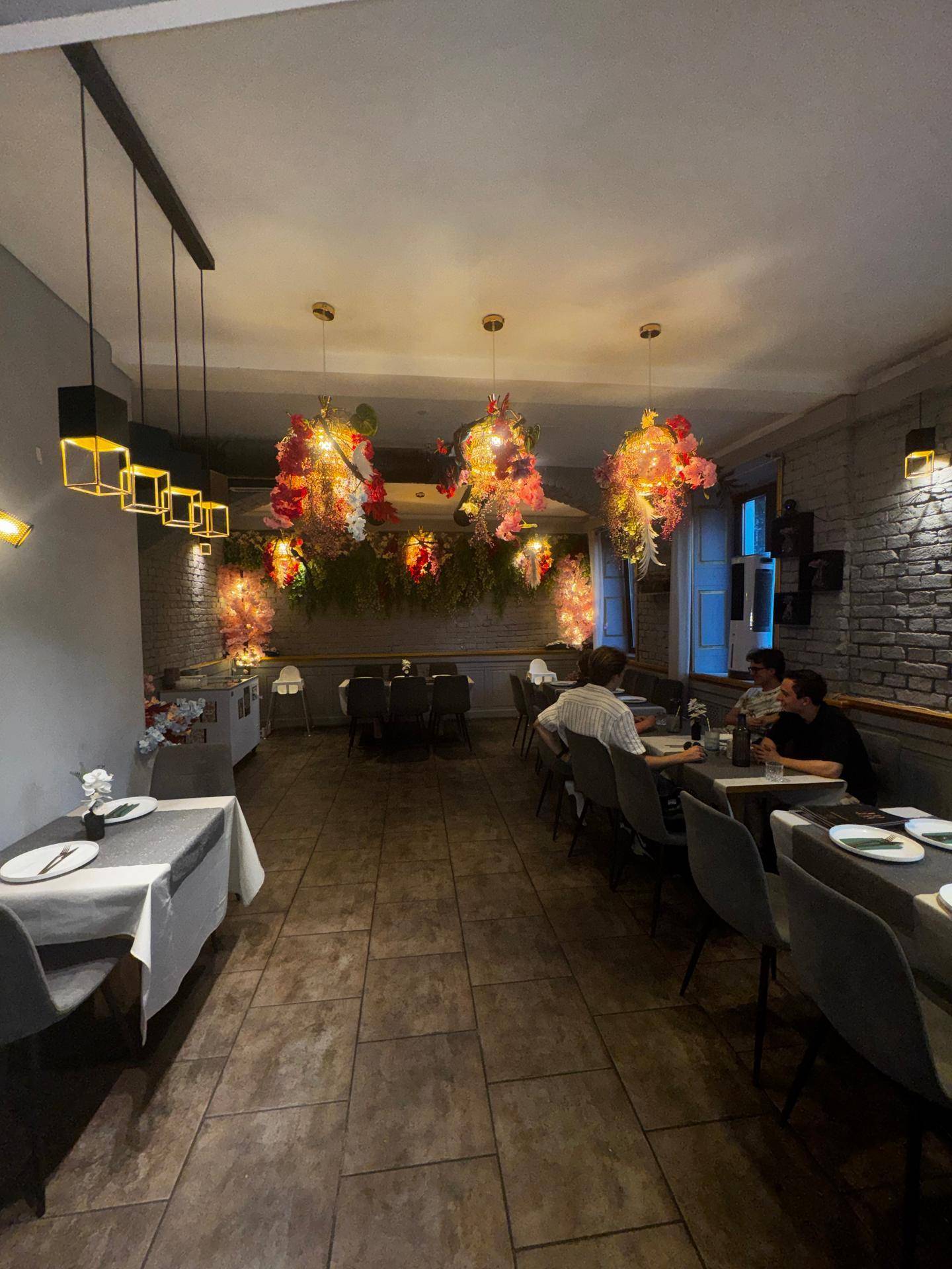 Restaurantbereich mit gedeckten Tischen, floraler Dekoration und stimmungsvoller Beleuchtung, die eine gemütliche Atmosphäre schafft.