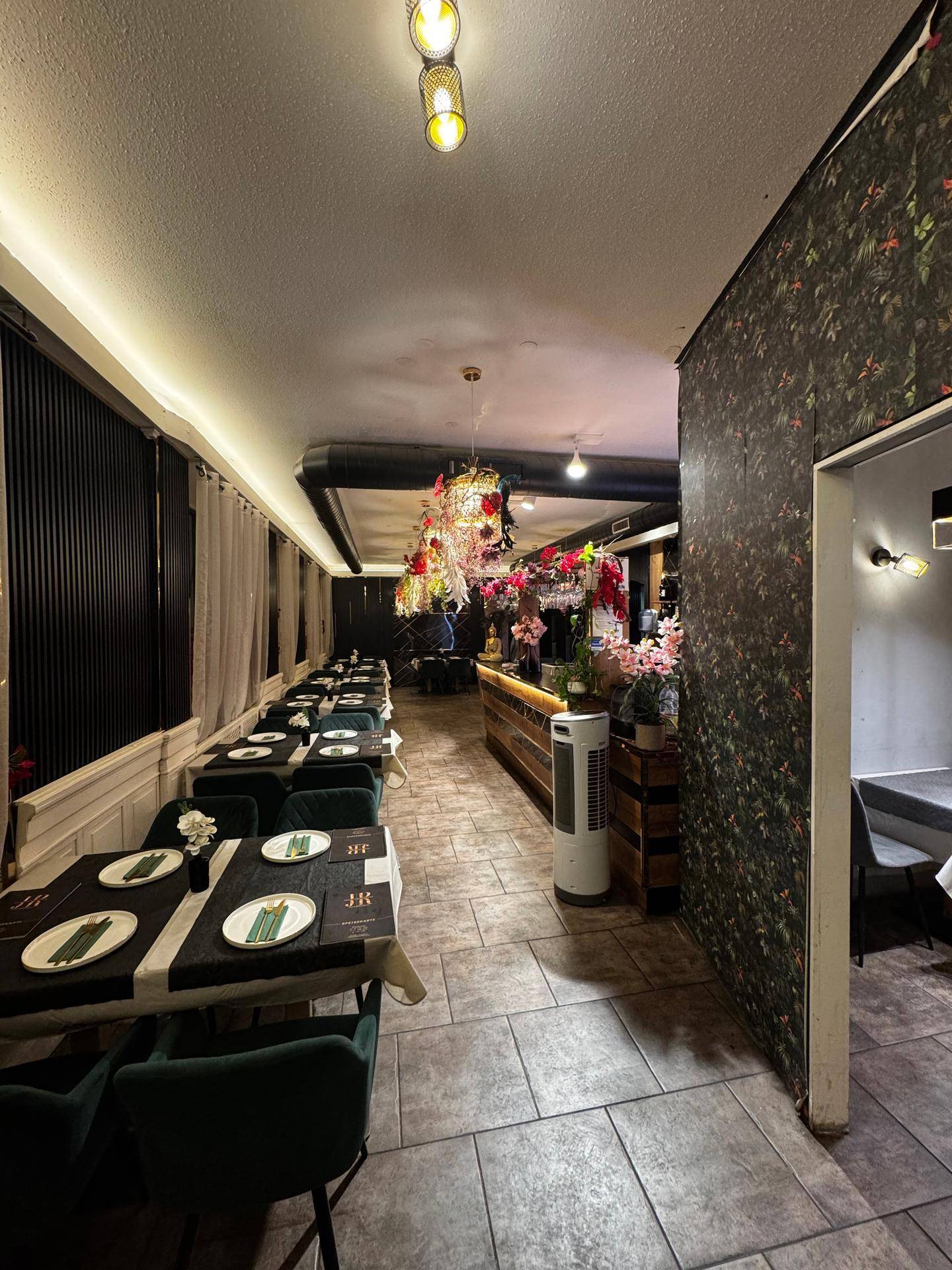 Restaurantinterieur mit gedeckten Tischen, Bar und floraler Dekoration an Wänden und Decke, die ein einzigartiges Ambiente schafft.