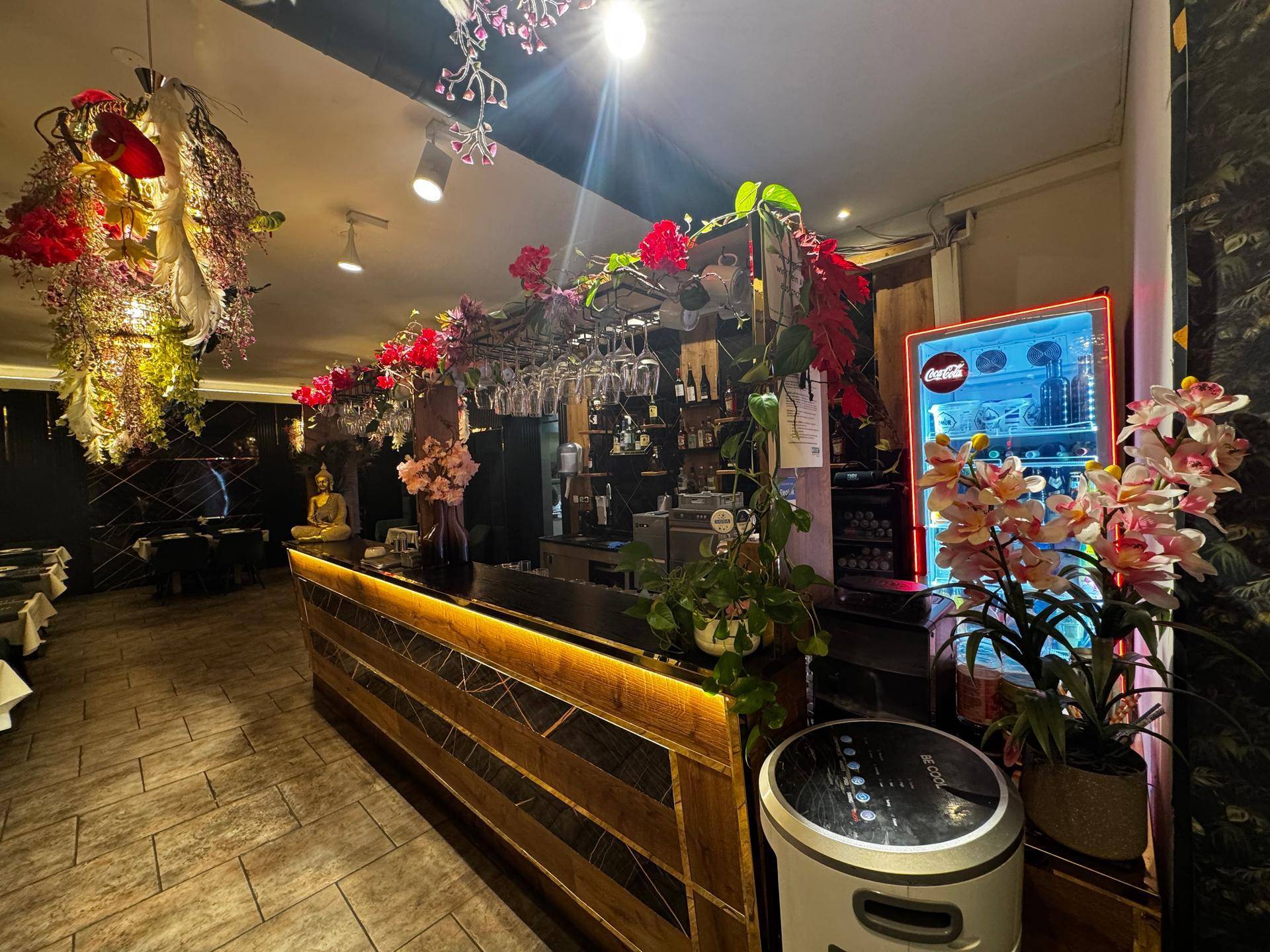 Detailansicht der beleuchteten Bar mit Getränken, Gläsern, einem Kühlschrank und üppiger Blumendekoration.
