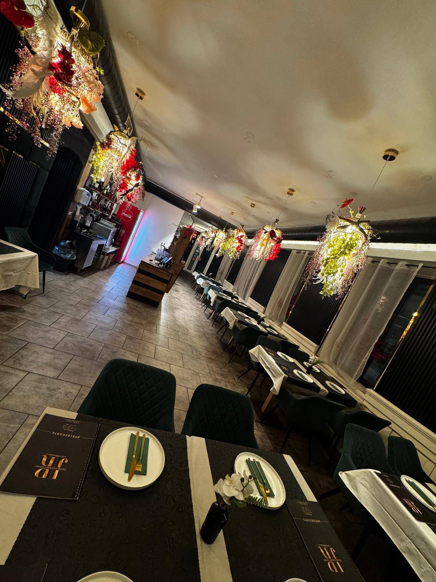 Weitwinkelaufnahme des Restaurantraums mit vielen Tischen und floraler Deckenverzierung, die den Raum belebt.