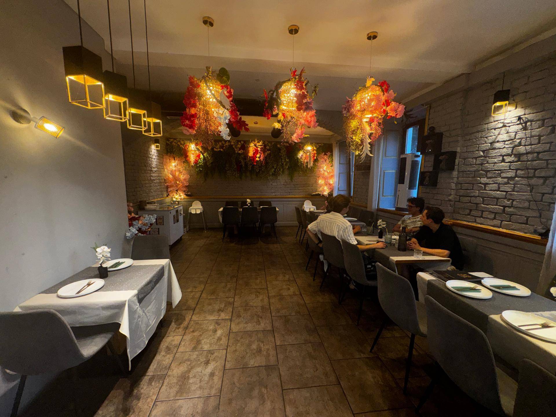 Restaurantinterieur mit Tischen, Stühlen und auffälligen floralen Deckenleuchten, die den Raum schmücken.