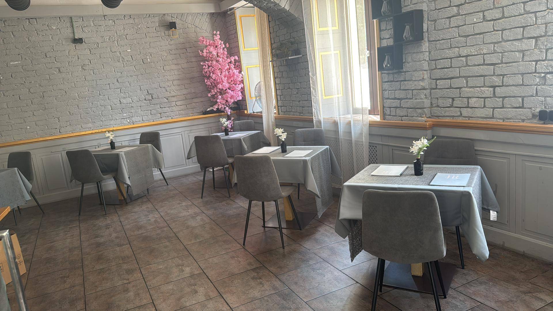 Geräumiger Speisesaal mit grauen Ziegelwänden, mehreren Tischen, grauen Stühlen und einem dekorativen rosa Baum.