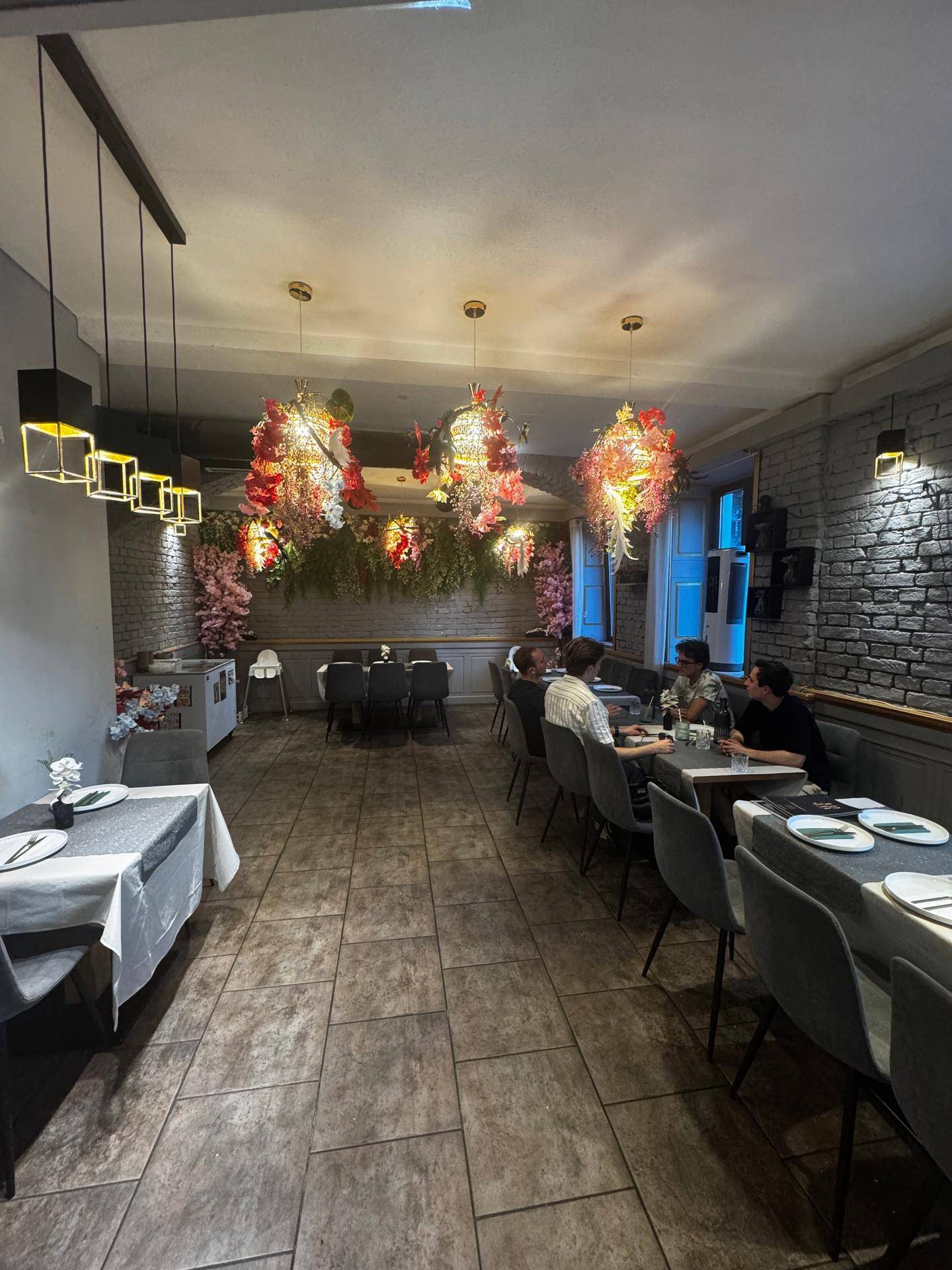 Restaurantinterieur mit Gästen an den Tischen, floraler Dekoration und indirekter Beleuchtung, die eine angenehme Stimmung erzeugt.