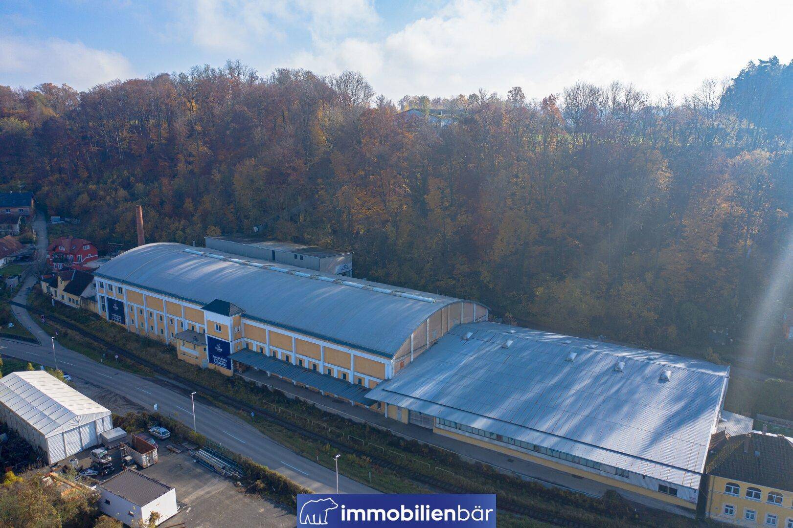 Luftaufnahme von zwei miteinander verbundenen Industriehallen mit gewölbten Dächern und umliegender Natur.