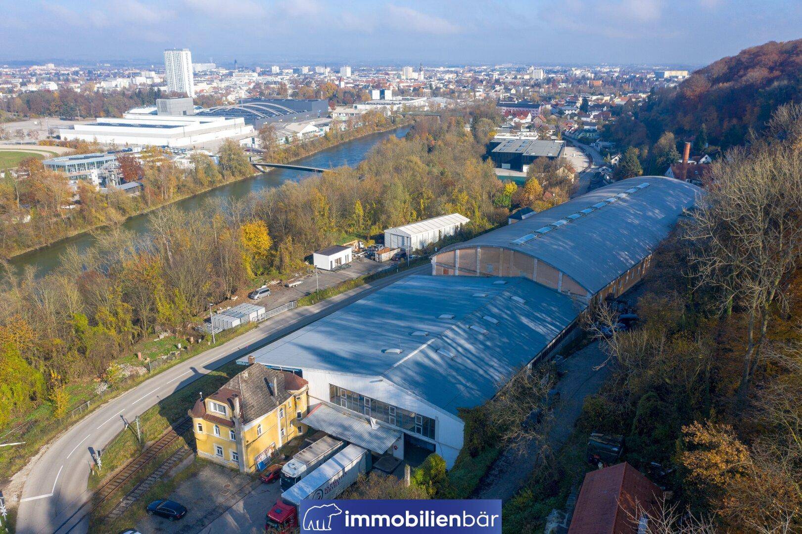 Weitläufige Luftaufnahme eines Industriegebäudes am Fluss mit Blick auf die Stadt im Hintergrund.