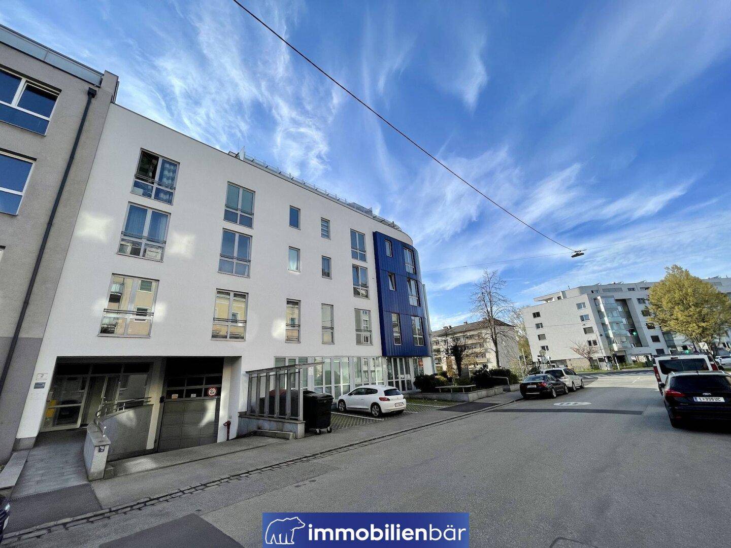 Ansicht des modernen Gebäudes mit Eingangsbereich und Parkplätzen unter blauem Himmel.