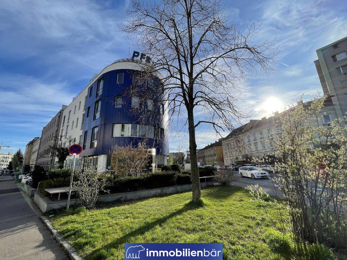 Modernes Gebäude mit blauer Fassadenverkleidung und Bäumen an einem sonnigen Tag.