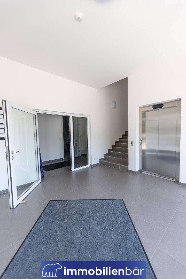 Heller Eingangsbereich mit Fliesenboden, Treppe und einem modernen Aufzug für bequemen Zugang zu den Etagen.