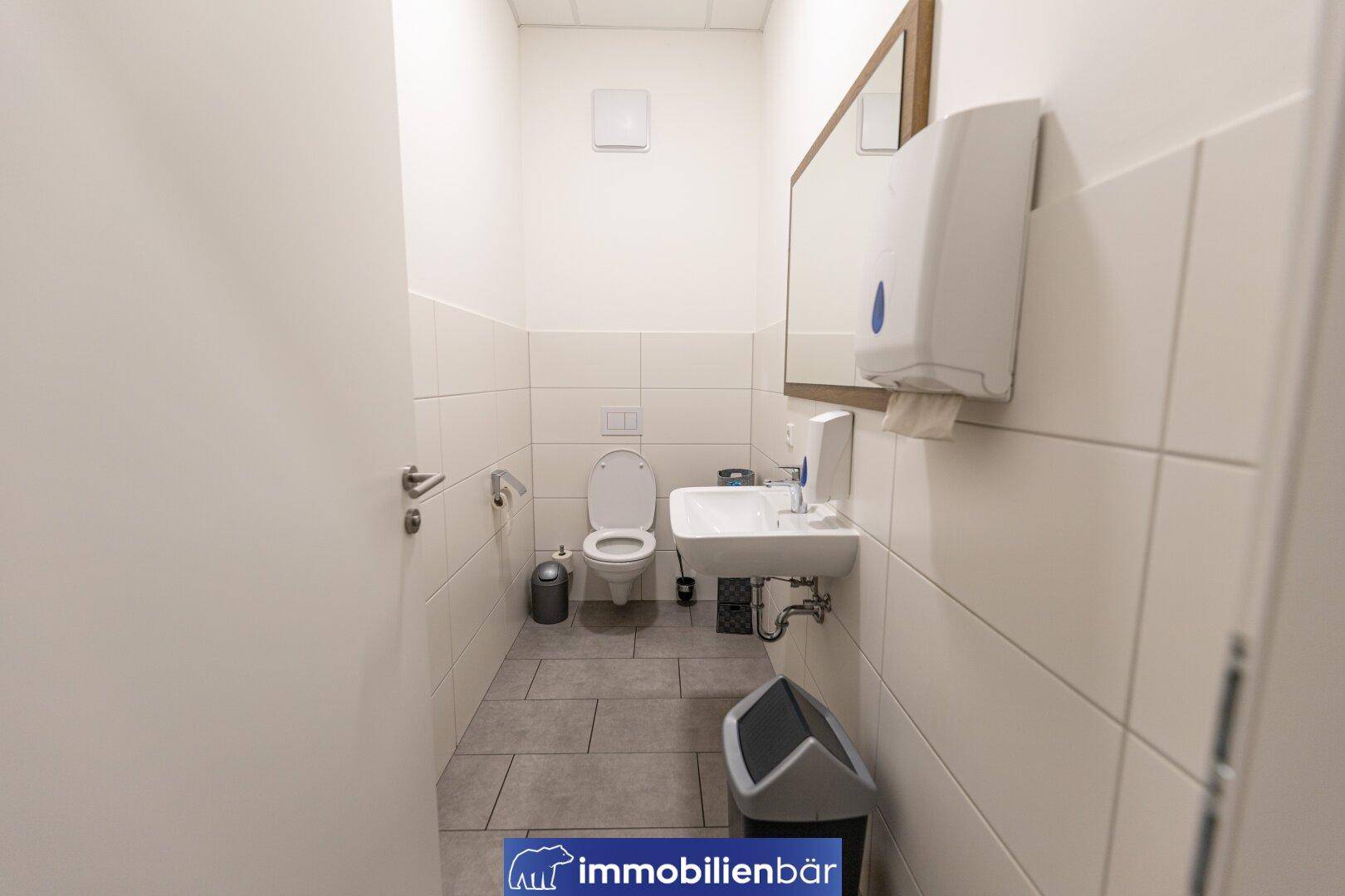 Sauberer Toilettenraum mit Waschbecken, Spiegel und Wandfliesen, ausgestattet für den gewerblichen Gebrauch.