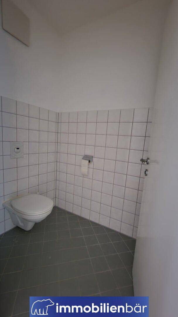 Separates WC mit wandhängender Toilette und Fliesenboden in neutralen Farben.