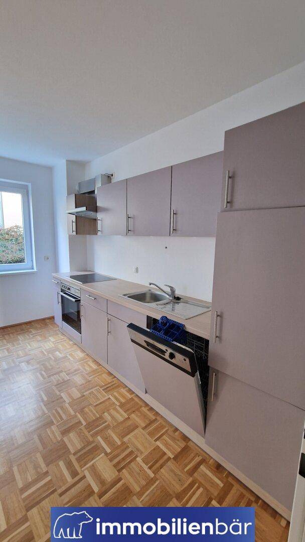 Helle Küche mit Einbaumöbeln, Fenster und Parkettboden, bereit zur Nutzung.