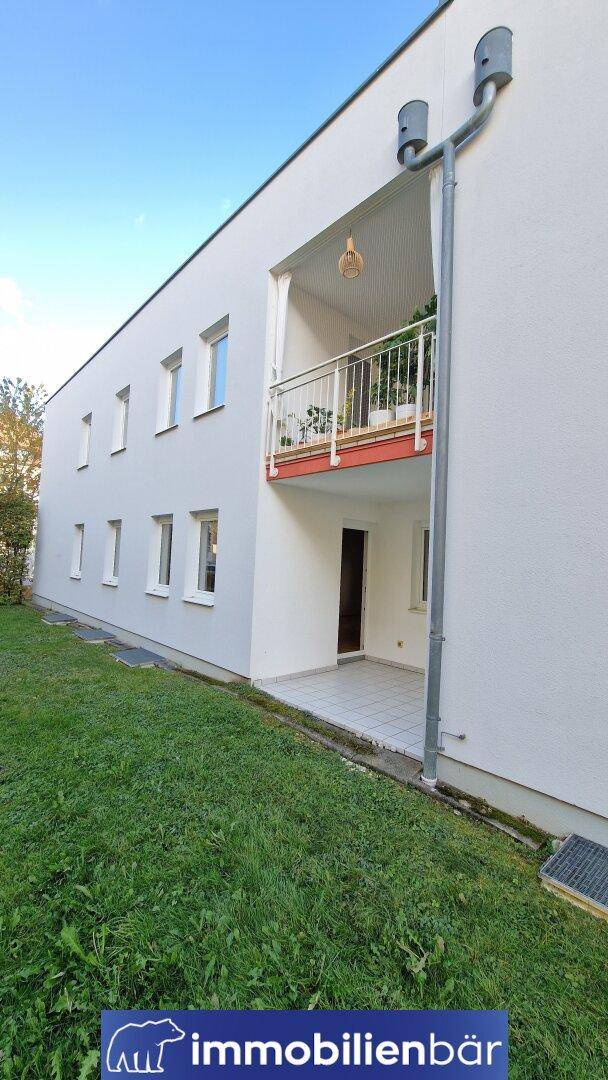 Moderne Gebäudefassade mit Loggia und direktem Zugang zur grünen Rasenfläche.