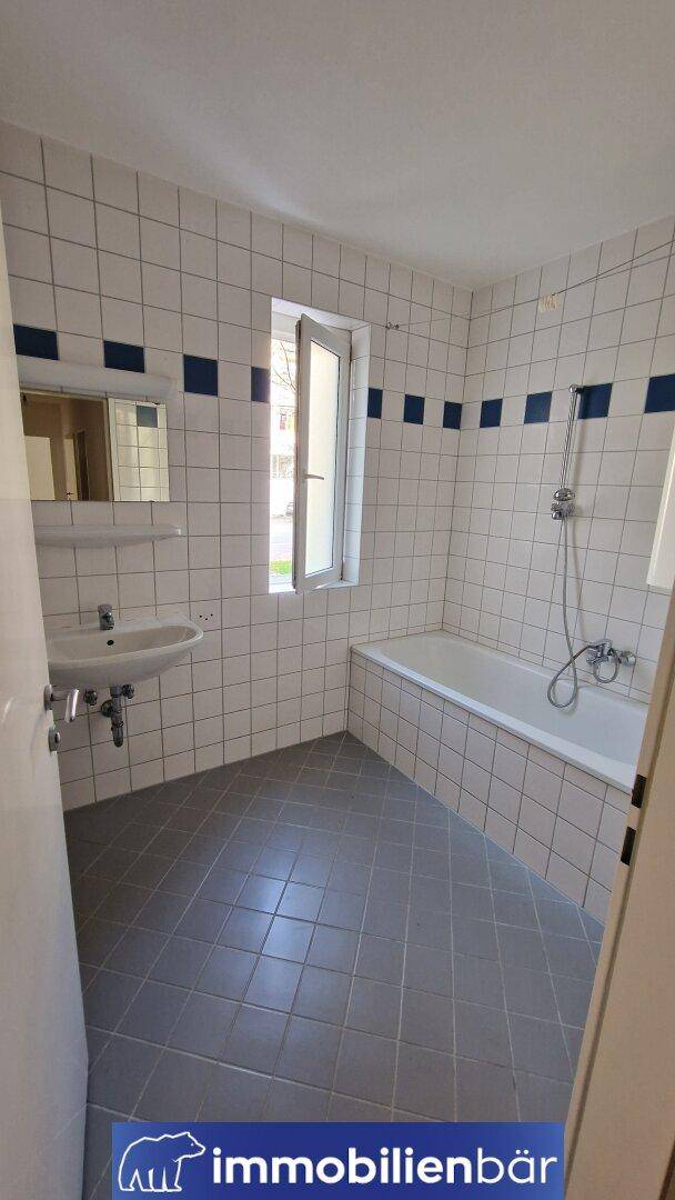 Gefliestes Badezimmer mit Badewanne, Waschbecken und Fenster für Tageslicht.
