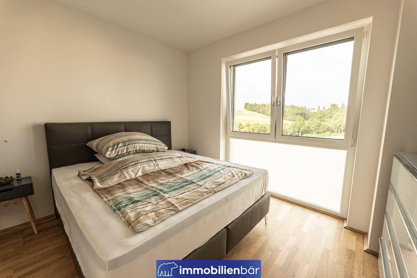 Gemütliches Schlafzimmer mit Doppelbett und großem Fenster, das viel Tageslicht und einen Blick ins Grüne bietet.