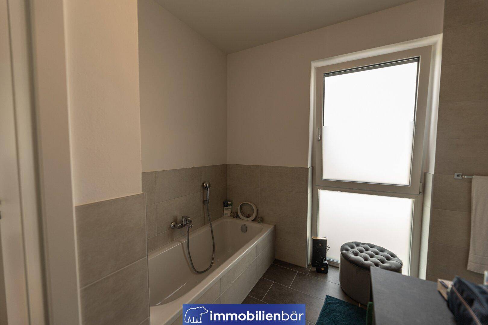 Modernes Badezimmer mit Badewanne, hellen Fliesen und einem Fenster für natürliche Belüftung und Tageslicht.