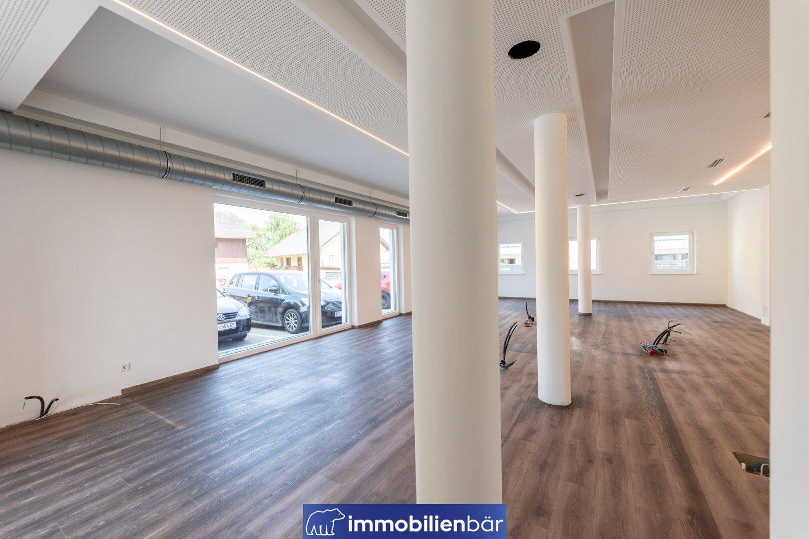 Weitläufiger Gewerberaum mit großen Schaufenstern, Säulen und moderner Beleuchtung, ideal für Ladenflächen.