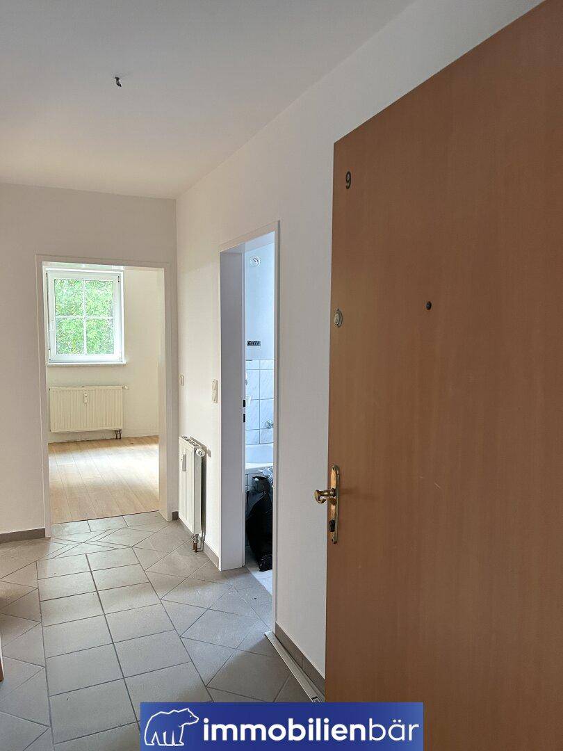 Heller Flur mit Fliesenboden, Zugang zu weiteren Räumen und einer Holztür.