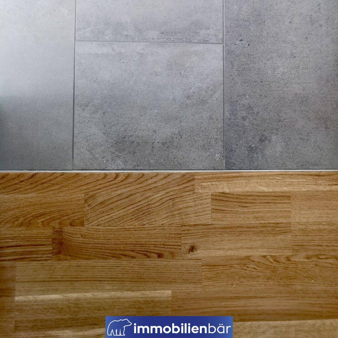 Detailaufnahme des Übergangs zwischen Fliesenboden und Parkettboden in einem Innenraum.