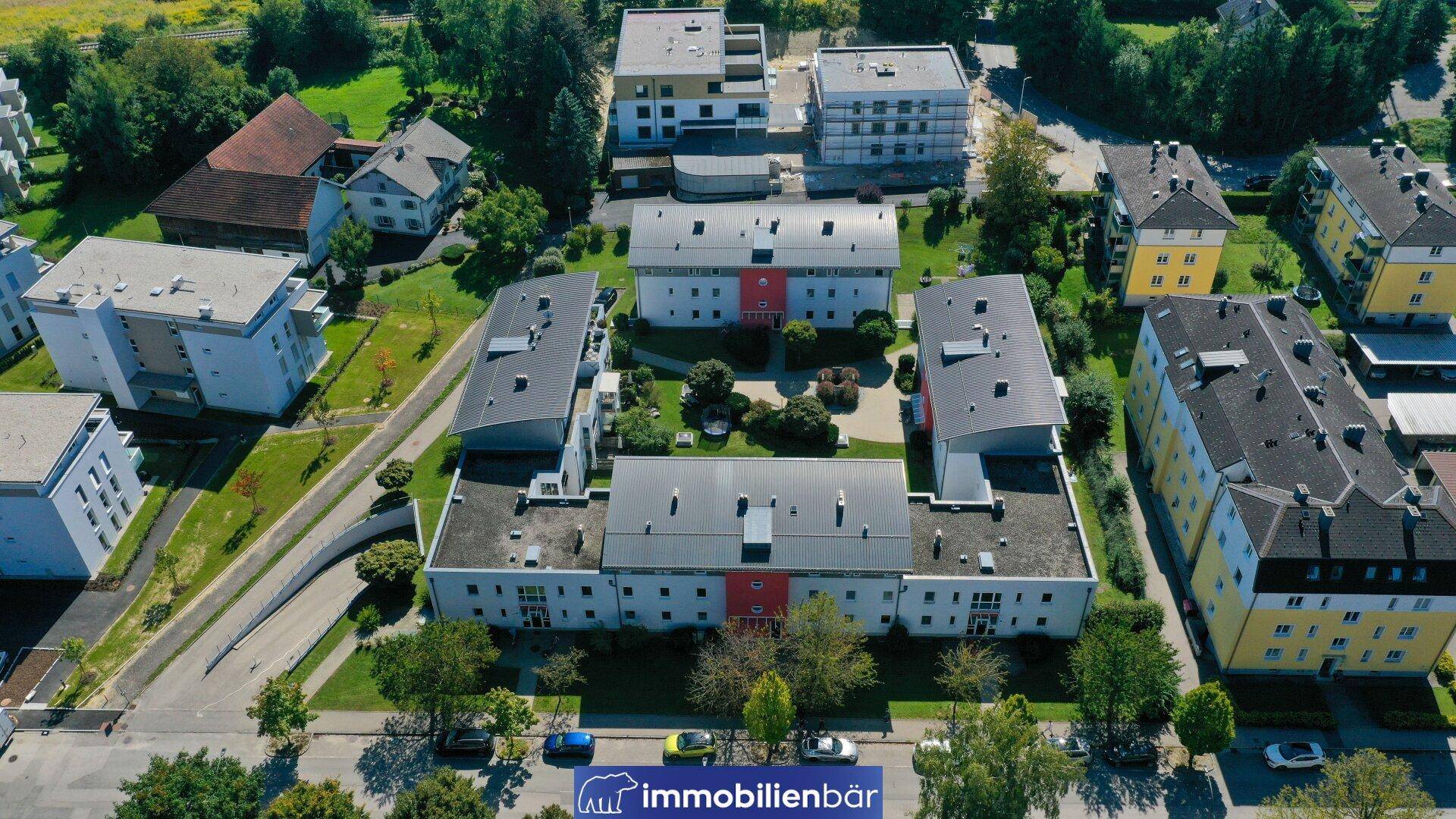 Luftaufnahme eines weitläufigen Wohnkomplexes mit mehreren Gebäuden und Grünflächen in einer Siedlung.