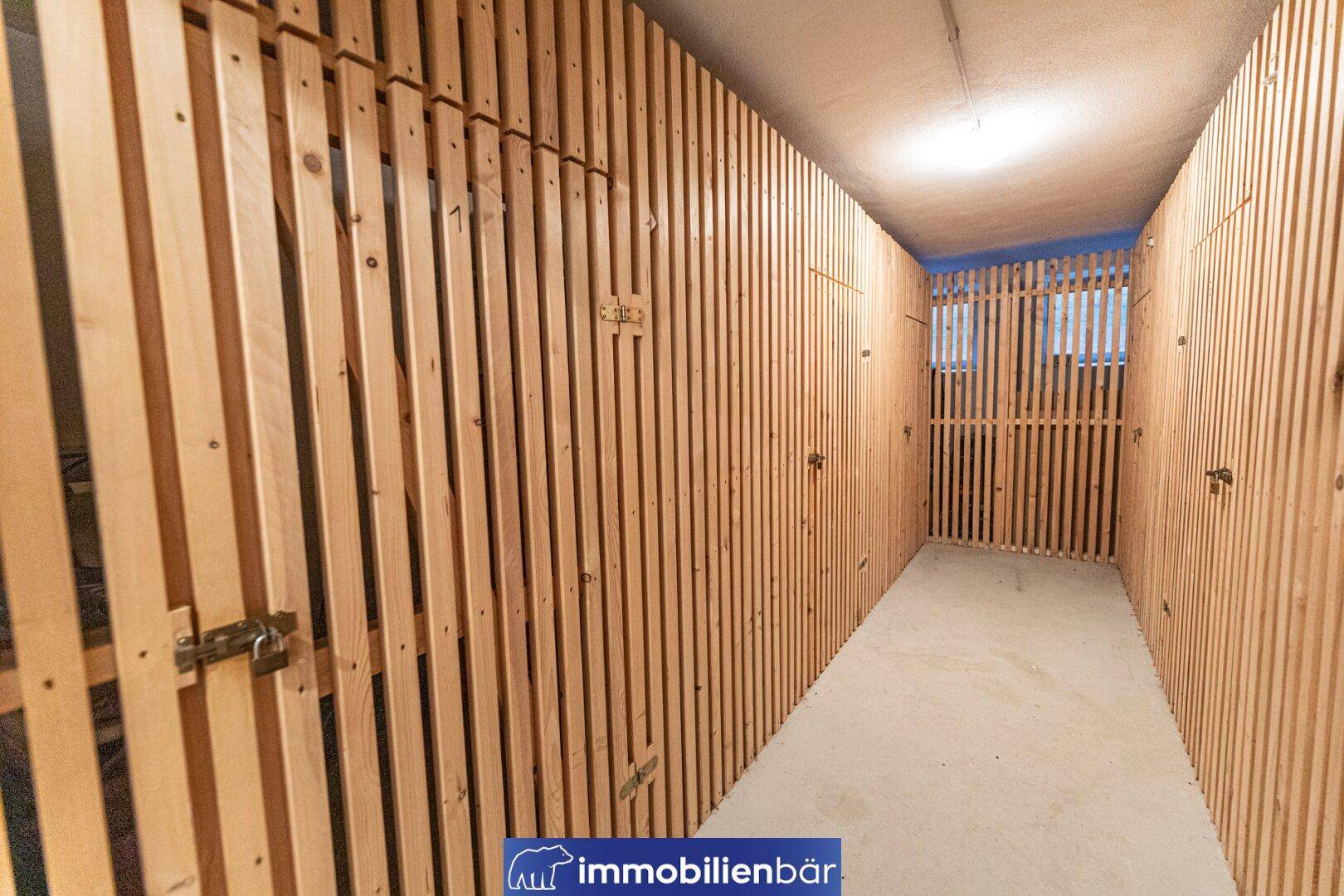 Gemeinschaftlicher Abstellraum mit Holzverschlägen für individuelle Lagermöglichkeiten im Kellerbereich.
