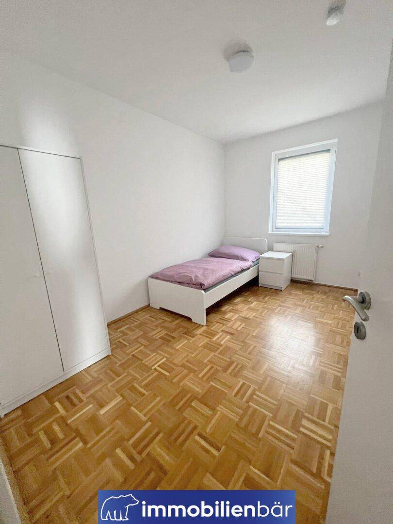 Helles Schlafzimmer mit Parkettboden, Einzelbett und weißem Kleiderschrank.